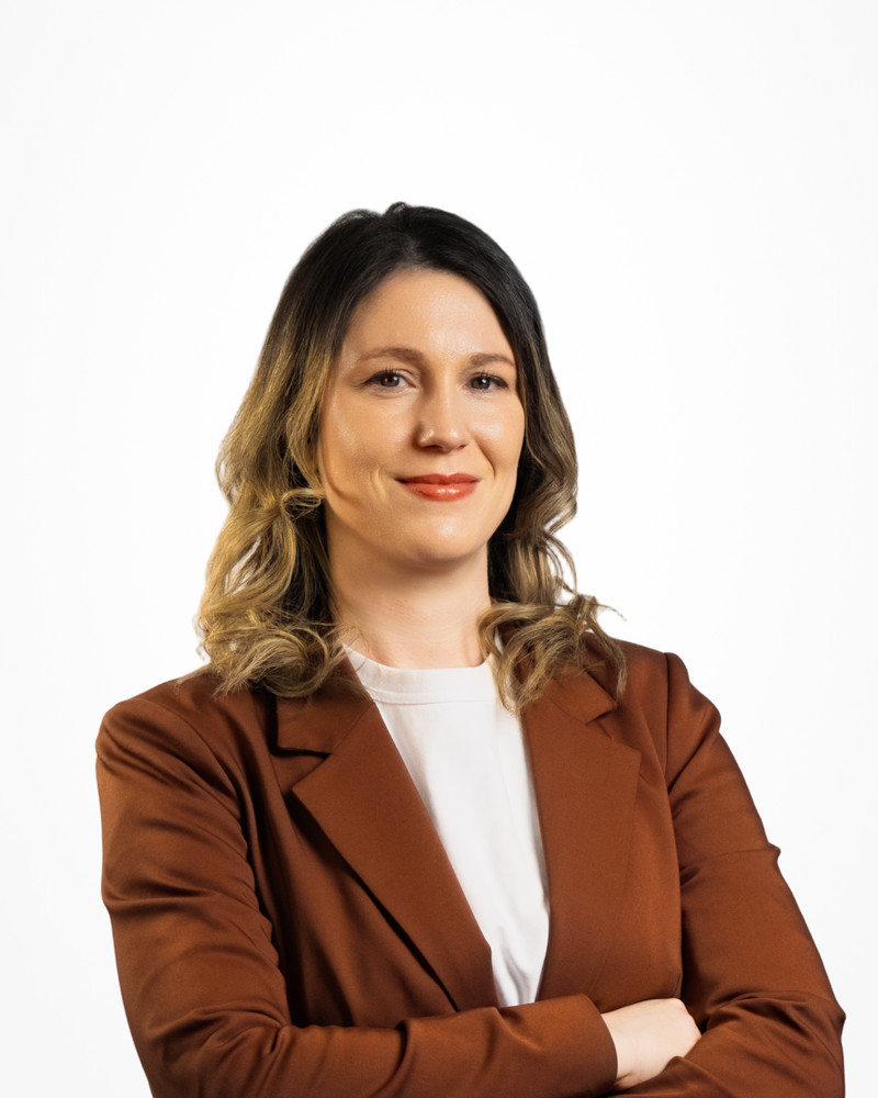 Corporate headshot of a woman in a rust-brown blazer on a white backdrop, photographed by Jay CS Films