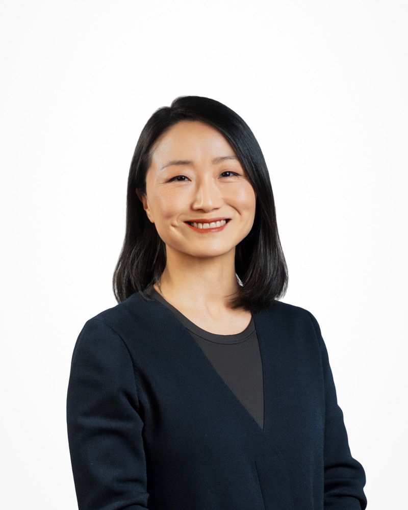 Corporate headshot of a smiling woman in a navy top on a white backdrop, photographed by Jay CS Films