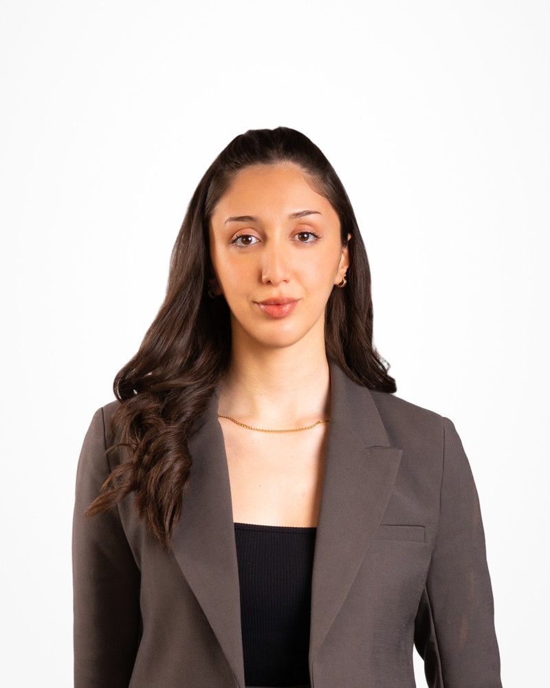 Corporate headshot of a woman with long dark hair in a taupe blazer on a white backdrop, photographed by Jay CS Films
