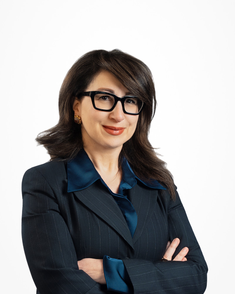 Corporate headshot of a woman with glasses in a navy pinstripe suit on a white backdrop, photographed by Jay CS Films