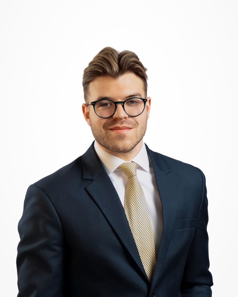 Corporate headshot of a man with glasses in a navy suit and gold tie on a white backdrop, photographed by Jay CS Films