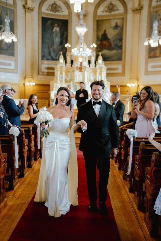 Bride and groom walking back down the red-carpet aisle of an ornate church as guests cheer, Montreal wedding photography