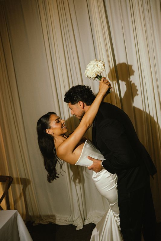 Groom dipping the bride as she raises her white bouquet against cream drapes, Montreal wedding photography